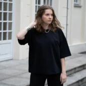 Czarna koszulka oversize z rękawem do łokcia, wykonana z bawełny. Modelka na zdjęciu łączy ją z czarnymi spodniami i grubą, srebrną biżuterią.
