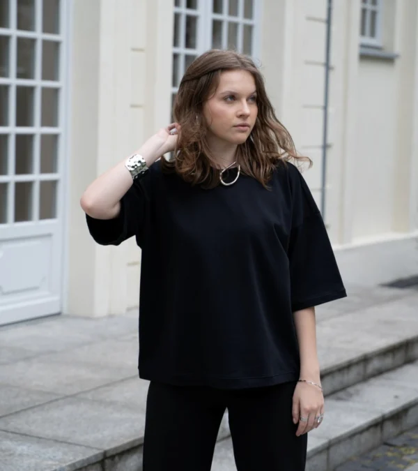 Czarna koszulka oversize z rękawem do łokcia, wykonana z bawełny. Modelka na zdjęciu łączy ją z czarnymi spodniami i grubą, srebrną biżuterią.